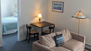 Una habitación acogedora con ventilador de techo, una mesita con sillas, un sofá con un cojín decorativo, una lámpara y un cuadro en la pared.