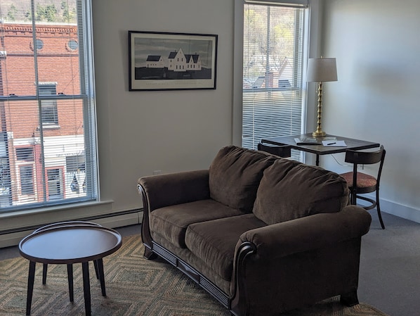 A living room with a brown sofa, a small round table, a lamp, and a framed picture on the wall. - Bristol Suites (Bristol)
