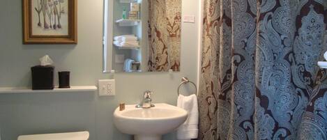Een badkamer met toilet, wastafel en spiegel. Op de muur hangt een ingelijste botanische illustratie, een handdoekhouder en decoratieve douchegordijnen.