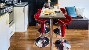 A modern kitchen with a dining area, featuring a table with red bar stools, a hanging light fixture, and artwork on the walls. - Allinkay Cusco Apart Hotel (Cusco)