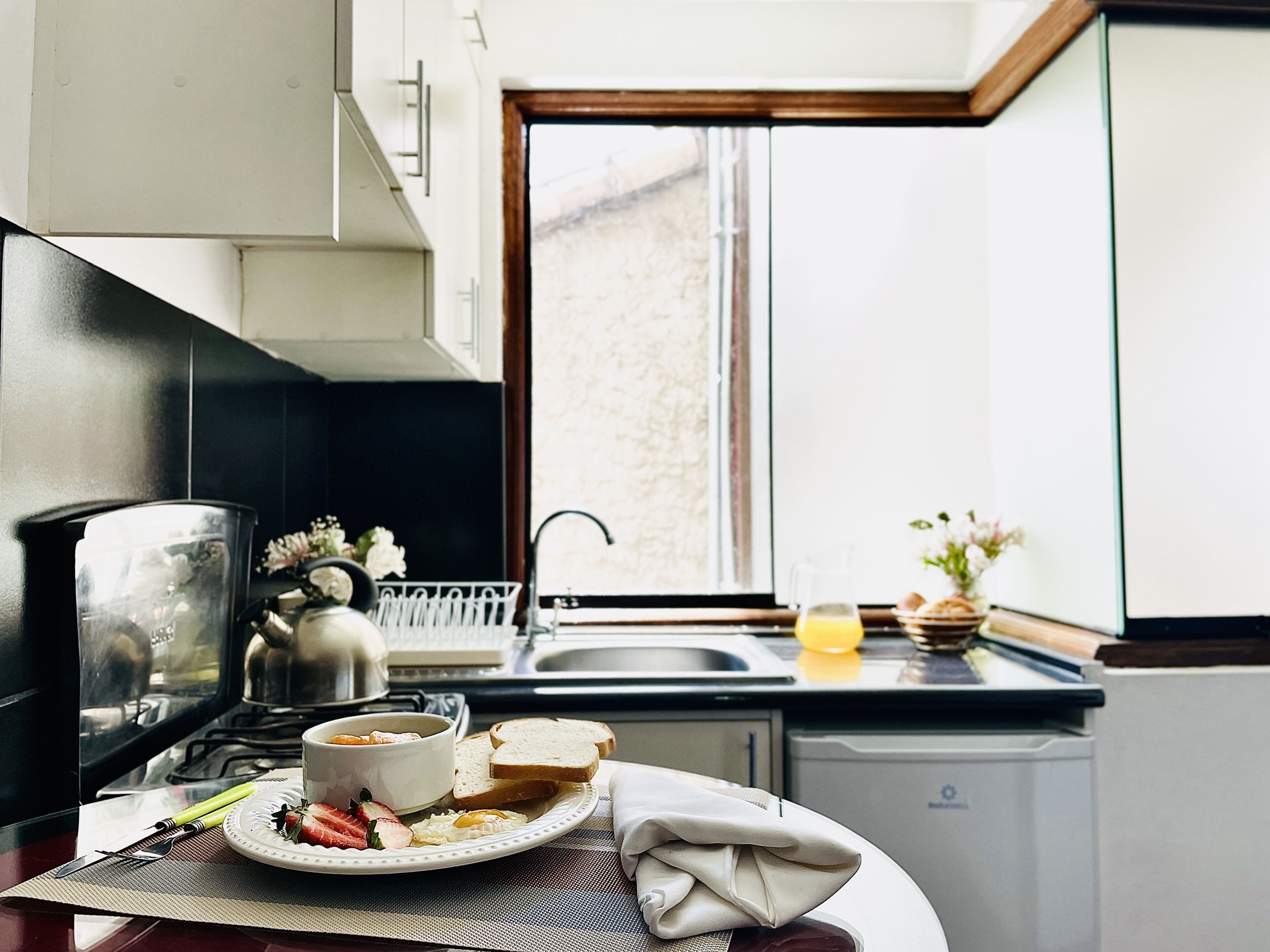 Una cocina con una mesa de comedor preparada para el desayuno, con huevos, tostadas y fruta.