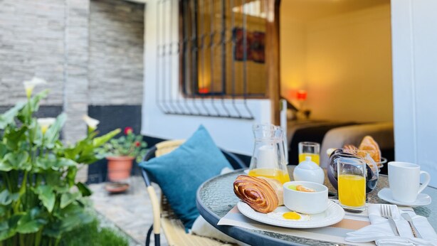A breakfast setup with croissants, eggs, and orange juice on a table outside a building with a stone wall and a window with metal bars. - Allinkay Cusco Apart Hotel (Cusco)