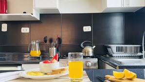 A modern kitchen with white cabinets, a black countertop, a kettle, and a glass of orange juice. - Allinkay Cusco Apart Hotel (Cusco)