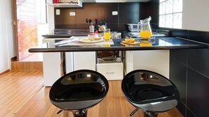 A modern kitchen with white cabinets, a black countertop, and two black bar stools. - Allinkay Cusco Apart Hotel (Cusco)