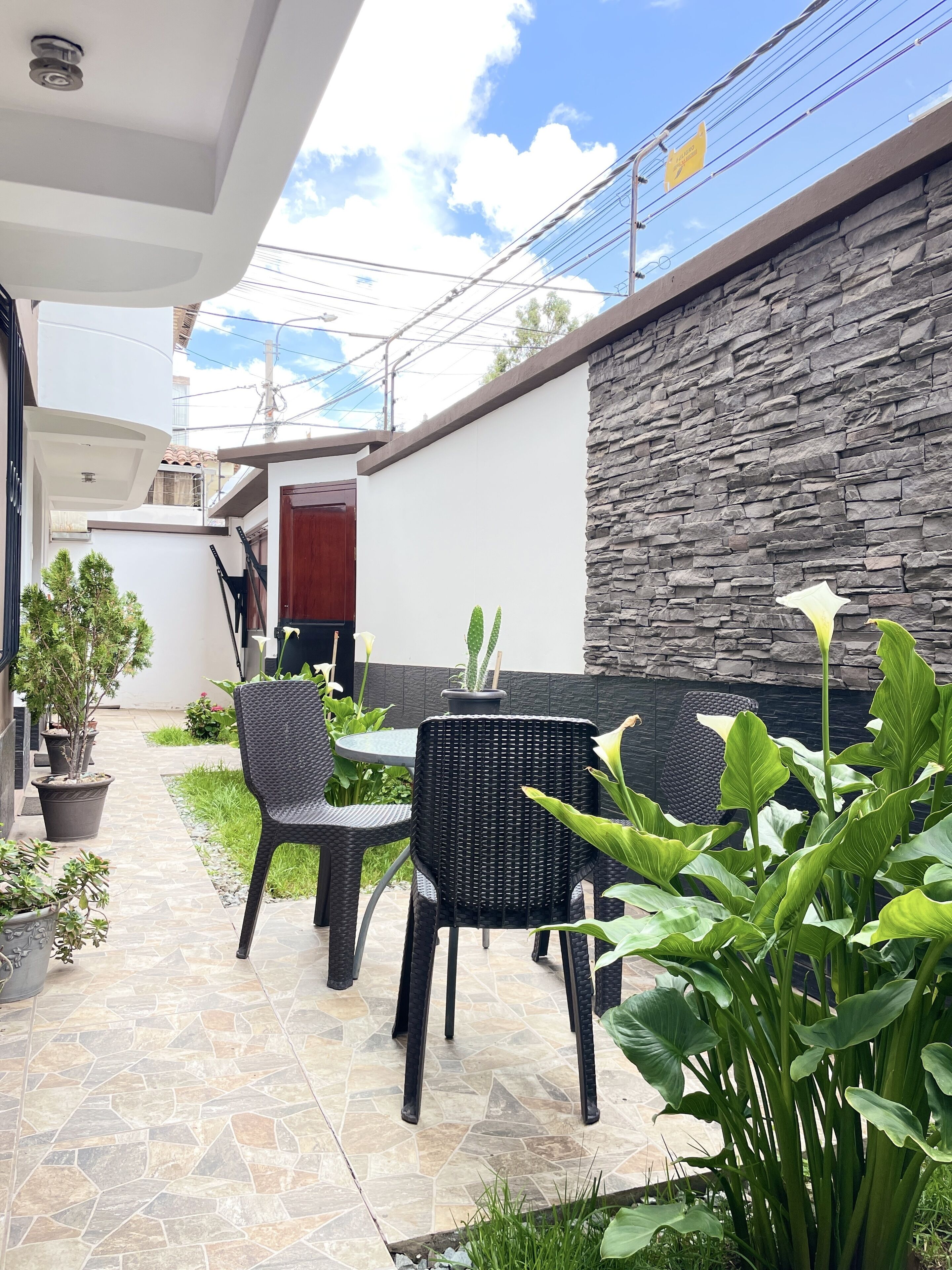A patio area with a stone-tiled floor, black wicker furniture, and potted plants.