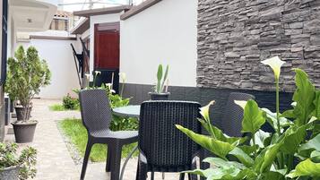 Un patio con suelo de baldosas de piedra, mobiliario de mimbre negro y plantas en macetas.