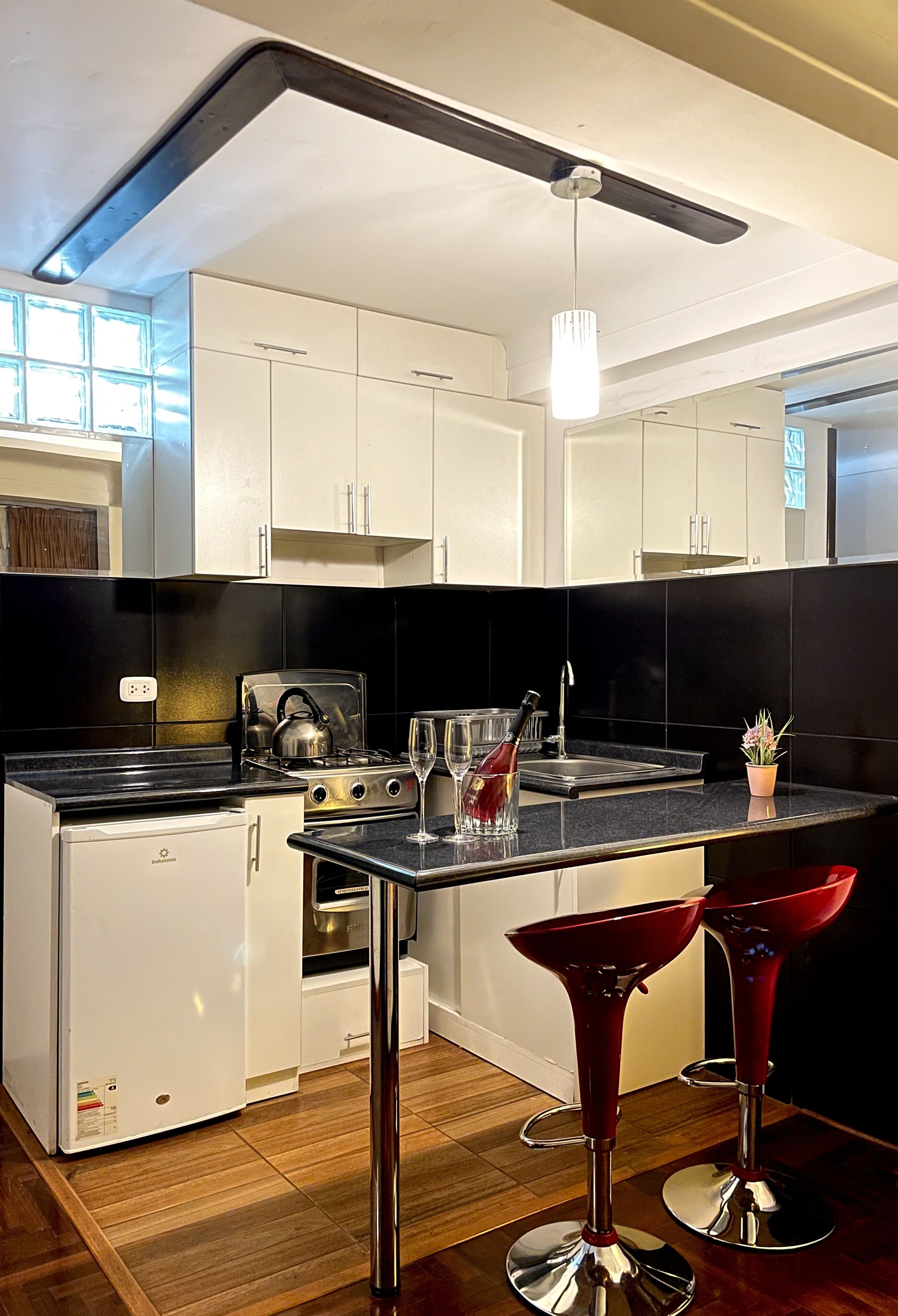 A modern kitchen with white cabinets, a black countertop, a built-in stove, and two red bar stools.