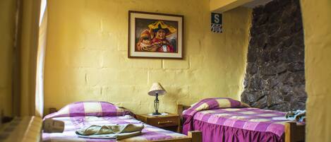 Une chambre avec deux lits, une table de chevet, une lampe, un tableau encadré au mur et un mur en pierre.