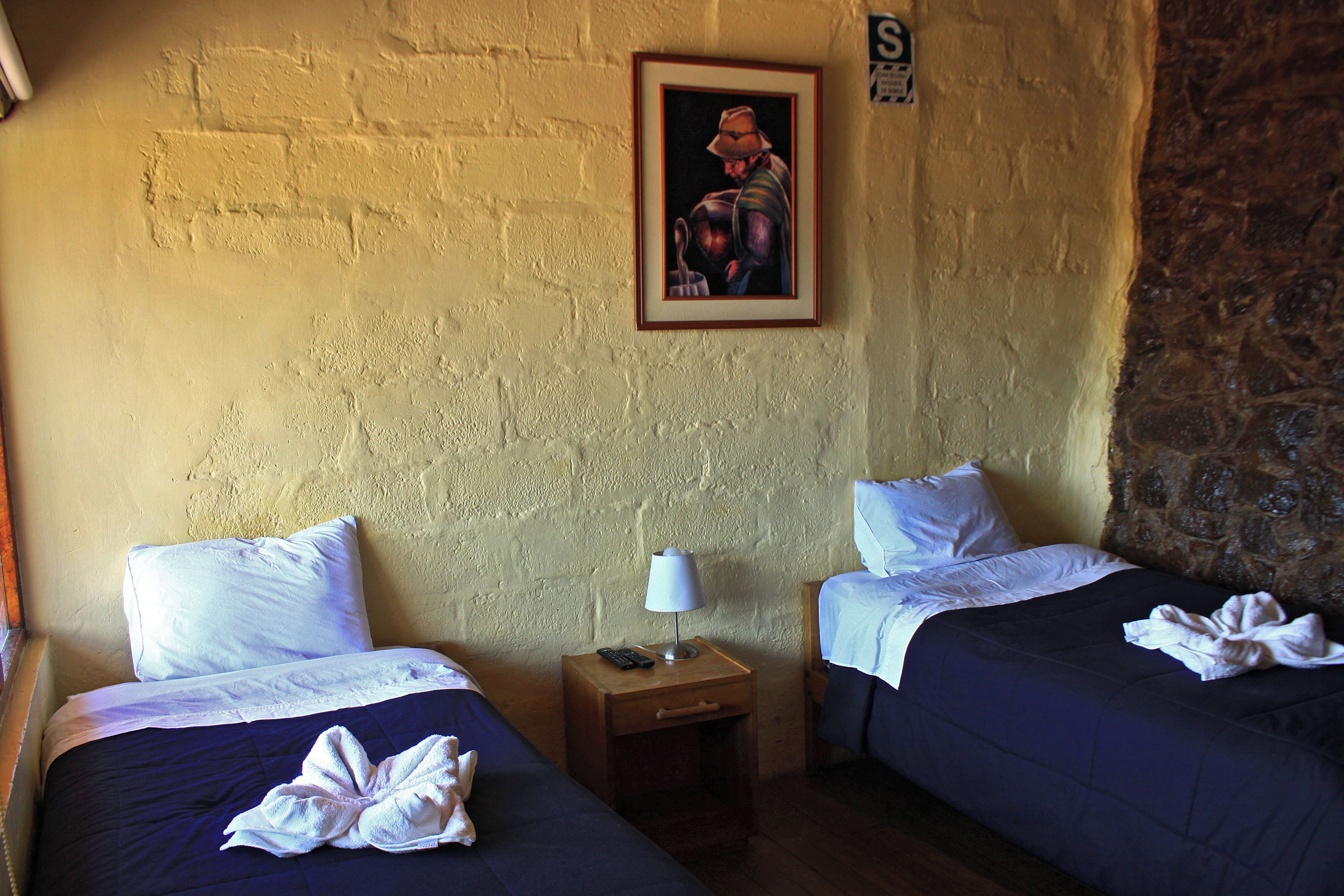 Una camera d'albergo con due letti, un comodino con una lampada e un quadro appeso al muro.