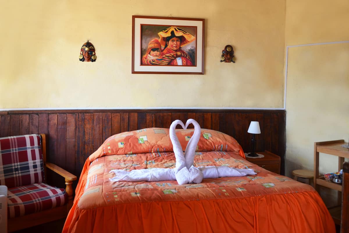 A hotel room with a bed, a chair, a nightstand, and a wall with a framed painting.
