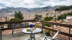 Un balcón con una mesa lista para dos personas, con vistas a un paisaje urbano y montañas al fondo.