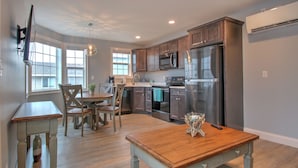 A modern kitchen with stainless steel appliances, wooden furniture, and large windows. - Atlantic Ocean Suites (Old Orchard Beach)