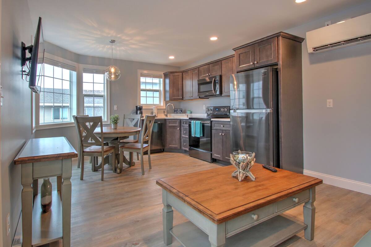 A modern kitchen with stainless steel appliances, wooden furniture, and large windows.