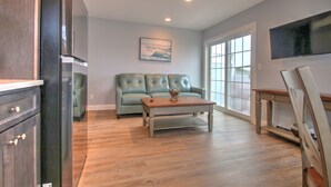 A spacious living room with hardwood flooring, a light green sofa, a coffee table, and a television mounted on the wall. - Atlantic Ocean Suites (Old Orchard Beach)