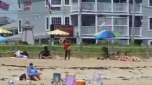 A large, multi-story building with a prominent American flag, likely a hotel or resort, situated on a beach with beach chairs and umbrellas. - Atlantic Ocean Suites (Old Orchard Beach)