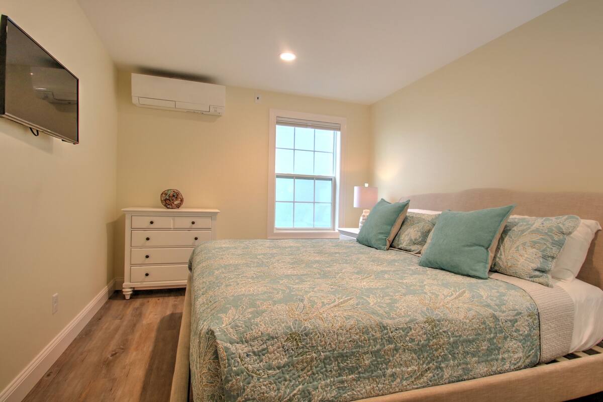 A bedroom with a bed, a dresser, a television, and a window.
