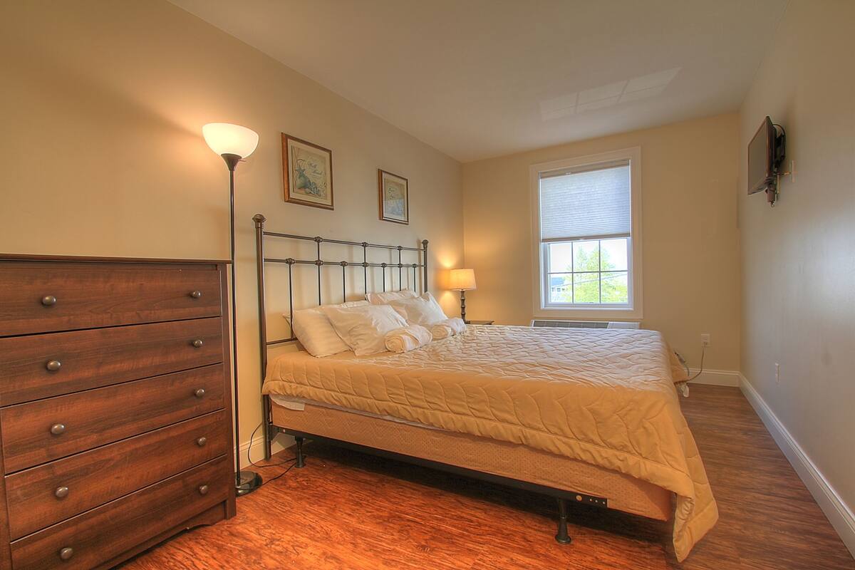 A bedroom with a bed, dresser, lamp, and window.
