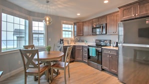A modern kitchen with wooden cabinets, stainless steel appliances, and a dining area with a round table and chairs. - Atlantic Ocean Suites (Old Orchard Beach)
