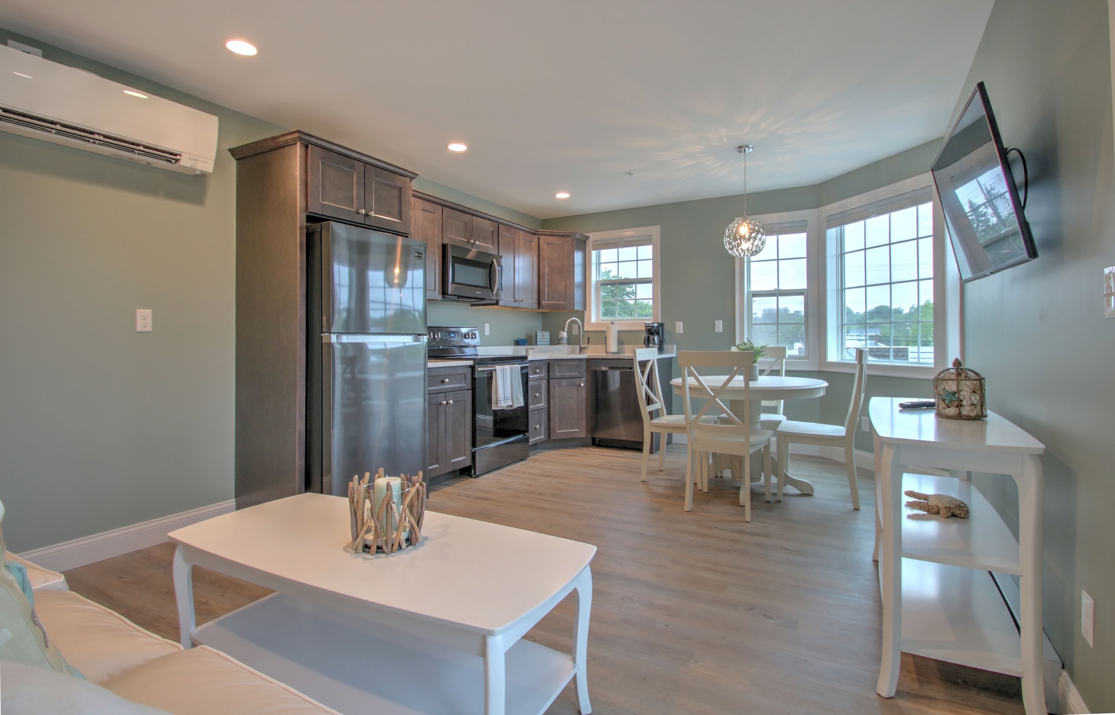 A modern kitchen with stainless steel appliances, a dining area with a white table and chairs, and large windows providing natural light.
