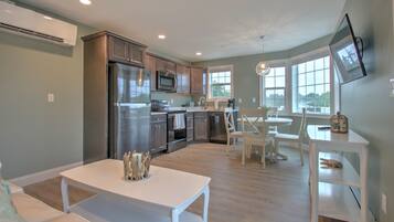 A modern kitchen with stainless steel appliances, a dining area with a white table and chairs, and large windows providing natural light.