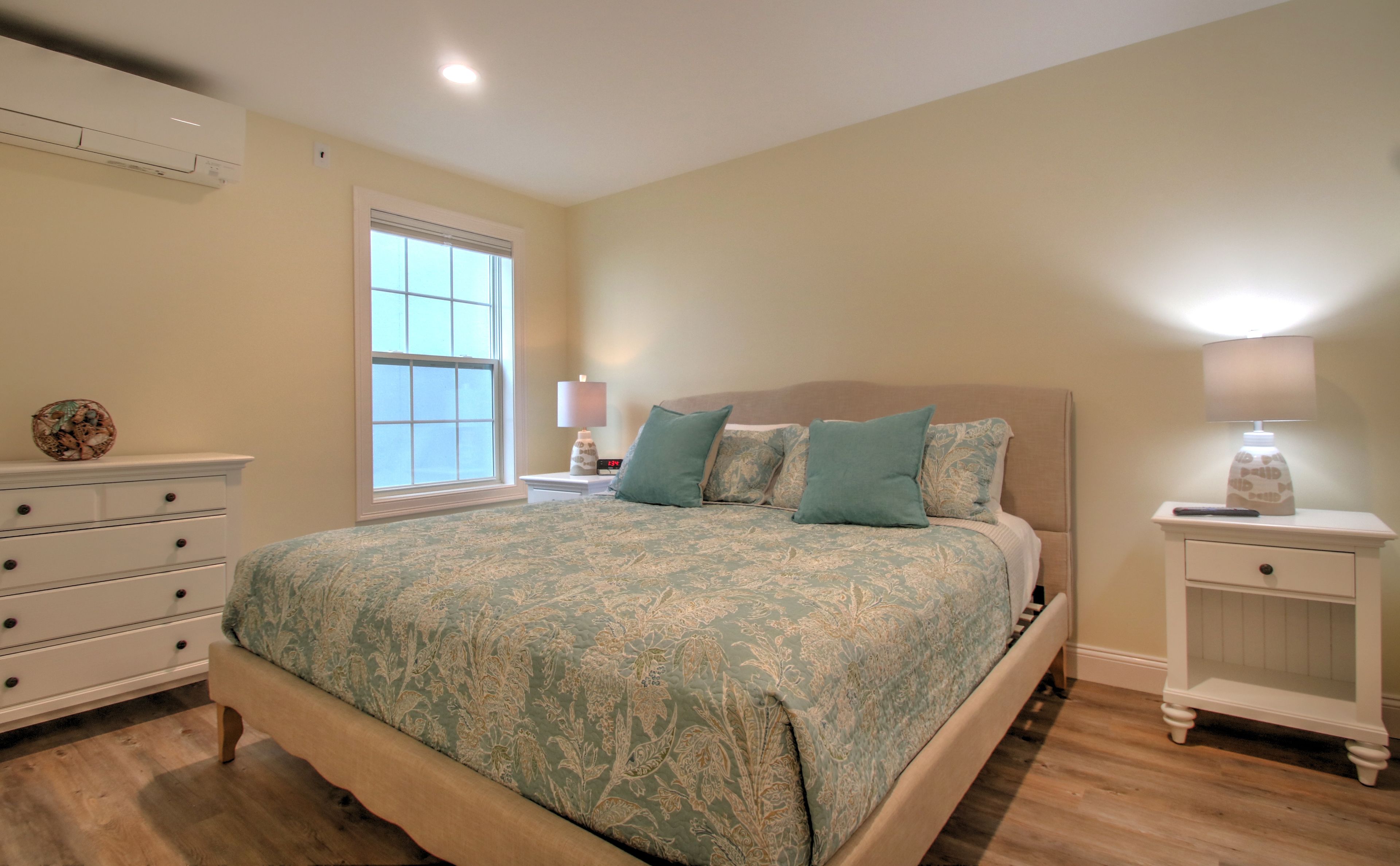 A bedroom with a large bed, a dresser, a nightstand, and a lamp.