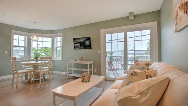 A spacious living room with a large window, a dining area with chairs, a white sofa, and a small table. - Atlantic Ocean Suites (Old Orchard Beach)
