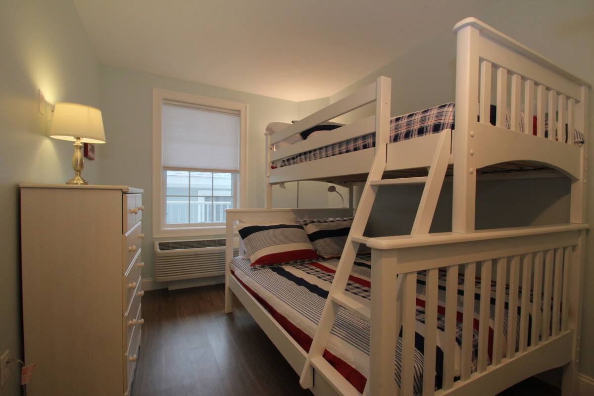 A bunk bed room with a window, a desk with a lamp, and a radiator.