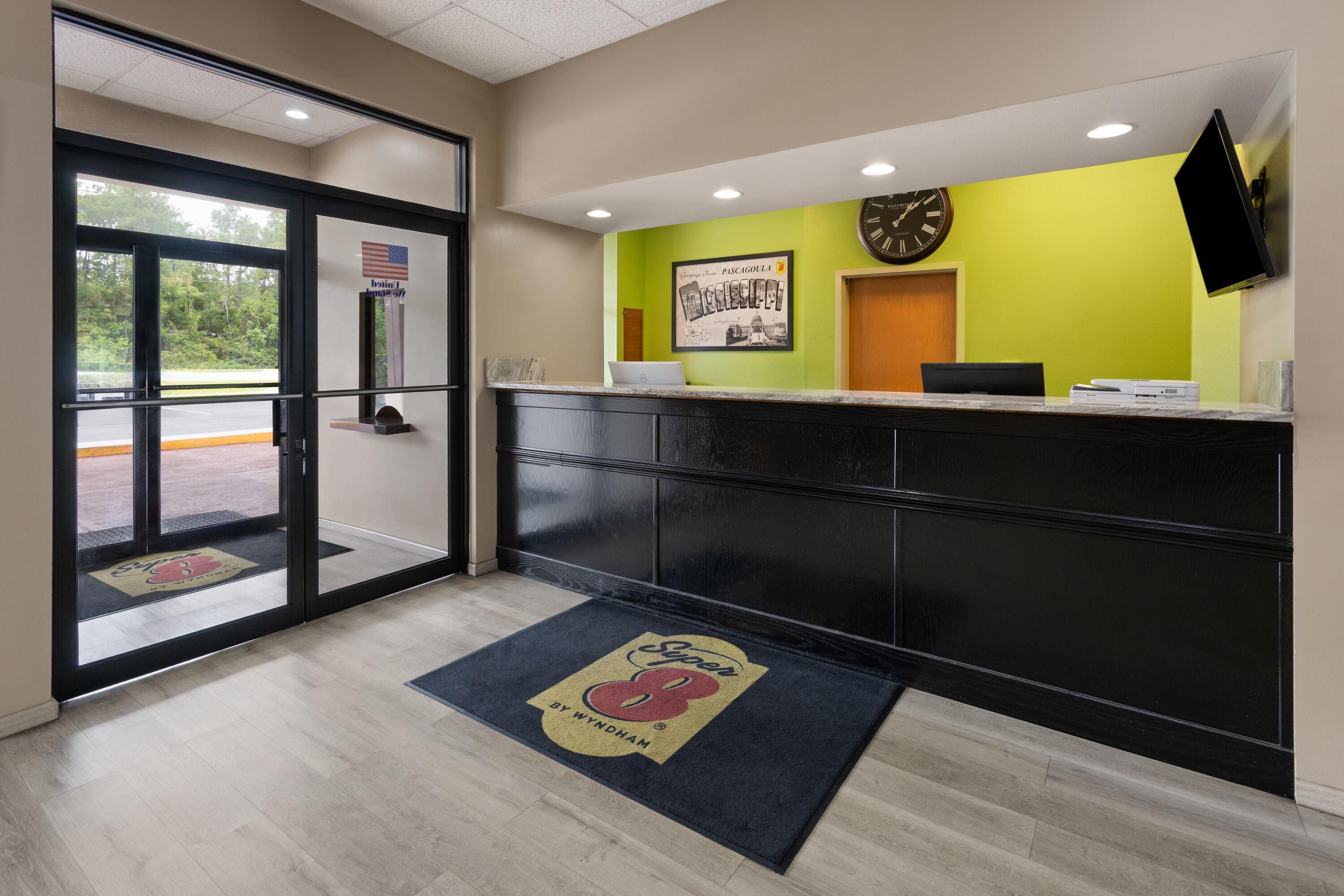 A reception area with a glass door, a reception desk, a clock, and a welcome mat.