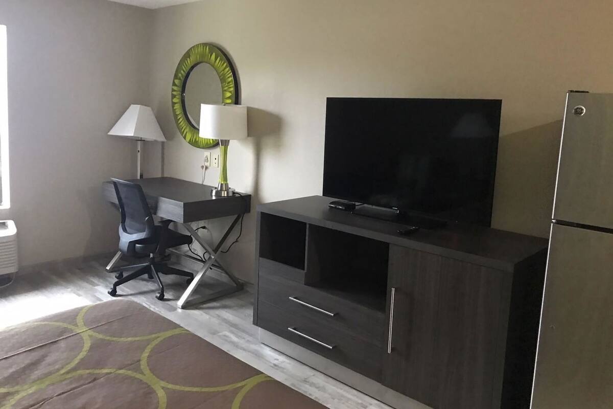 A modern hotel room with a desk, chair, TV, and refrigerator.