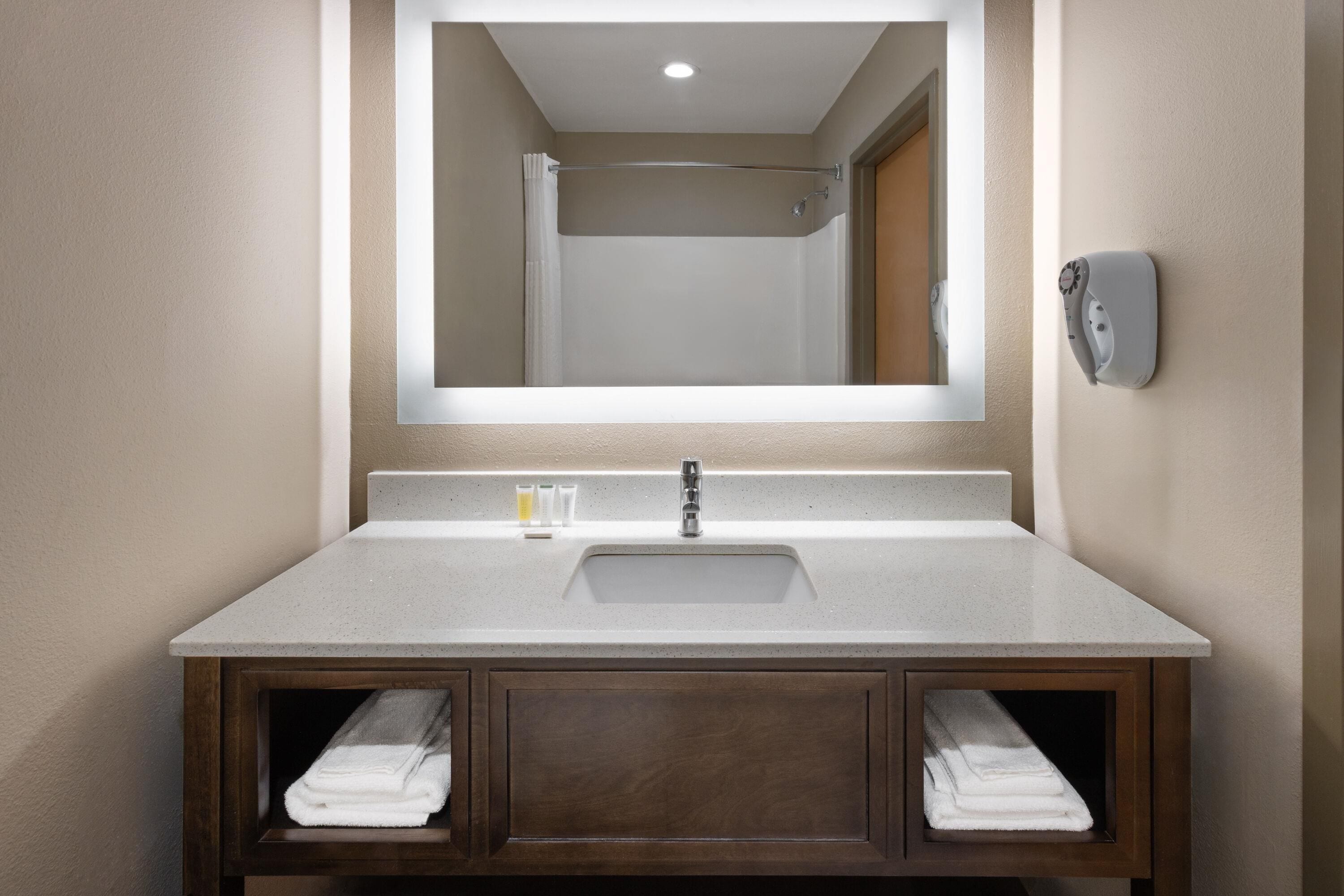 A bathroom with a large mirror, a sink, and a towel rack.