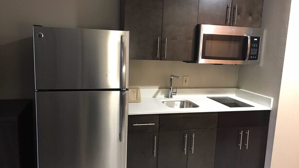 A kitchen with stainless steel appliances, a double sink, and dark cabinetry. - Super 8 by Wyndham Pascagoula (Pascagoula)