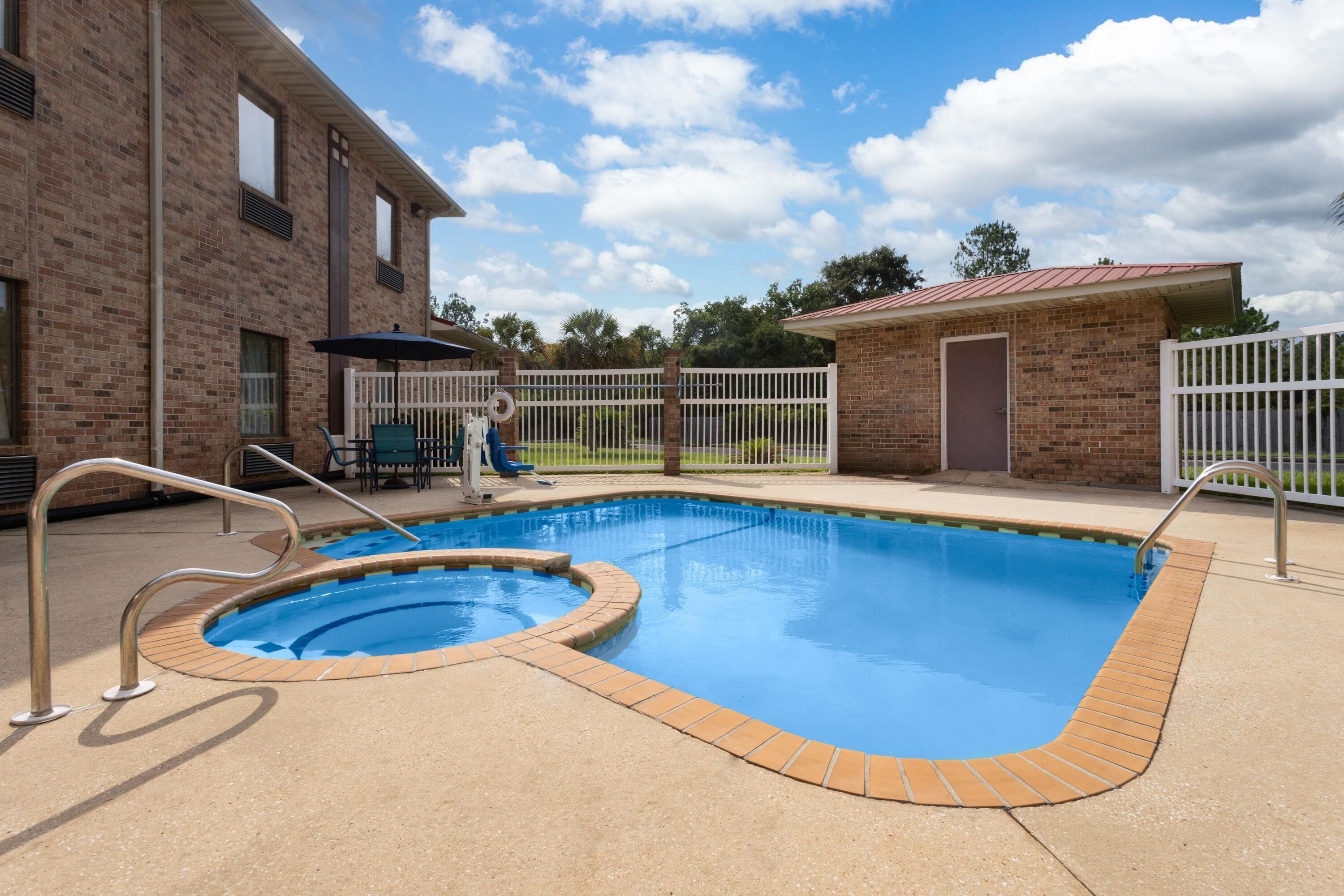 Une piscine avec une terrasse en briques, un patio clos et un petit bâtiment doté d’un toit rouge.