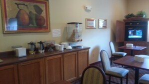A dining area with wooden tables and chairs, a coffee station, and a television on a stand. - Super 8 by Wyndham Pascagoula (Pascagoula)