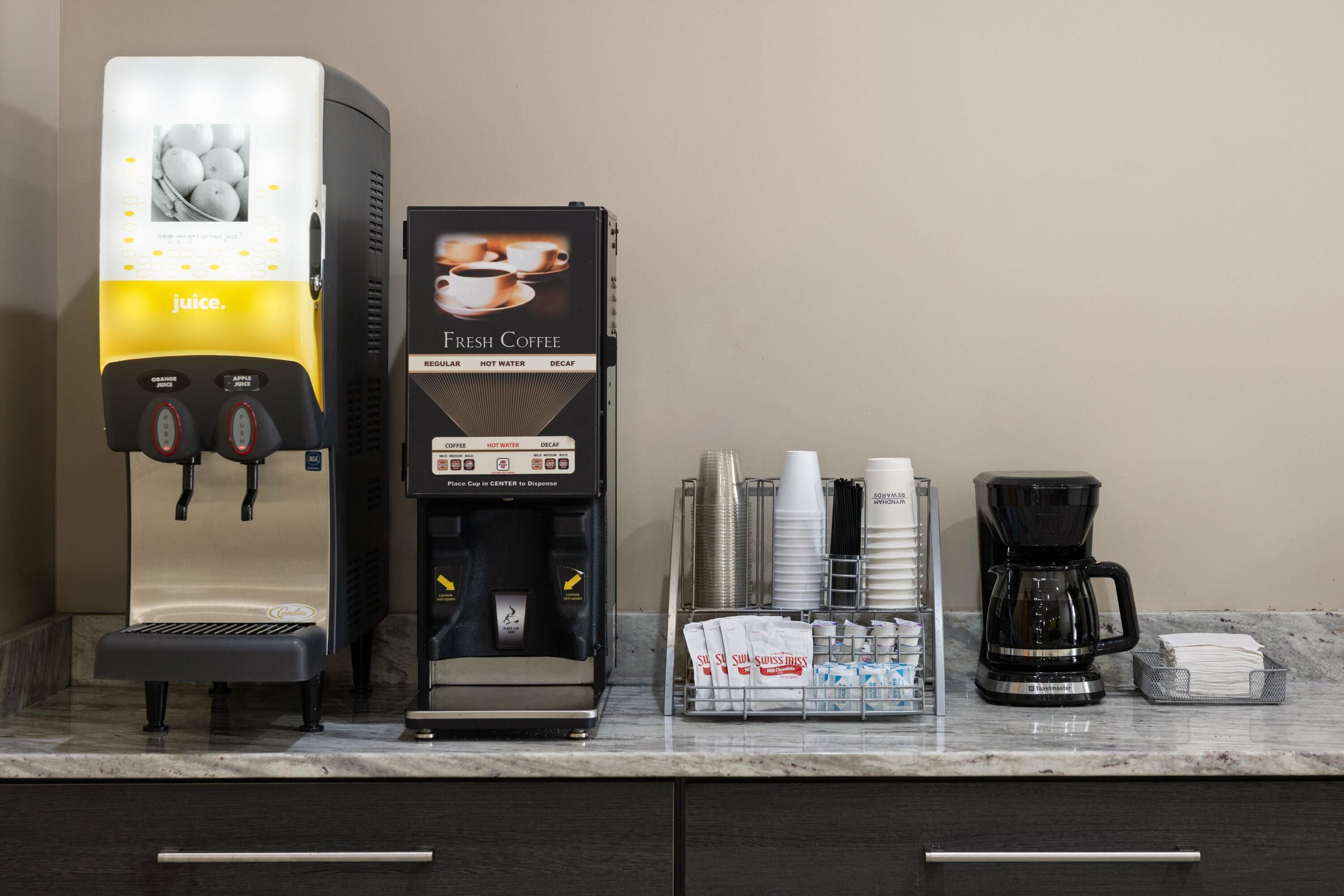 A coffee station with a juice dispenser, a coffee machine, and a coffee maker on a marble countertop.