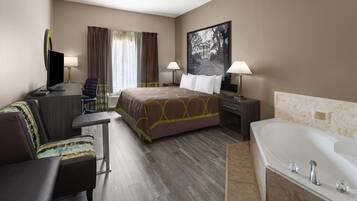 A hotel room with a bed, a desk, a chair, a TV, a lamp, a painting, and a bathtub.