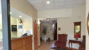 A reception area with a wooden desk, a reception phone, a clock, and a sign indicating the lobby. - Super 8 by Wyndham Pascagoula (Pascagoula)