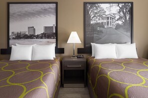 Habitación de hotel con dos camas, una mesita de noche, una lámpara y dos cuadros en la pared.