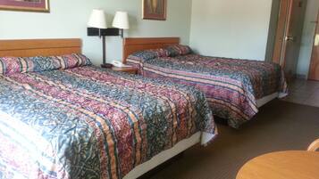A hotel room with two beds, each with patterned bedding, a bedside table with lamps, and a painting on the wall.