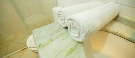 A bathroom with a white sink, a toilet, and two rolled towels on a marble countertop.