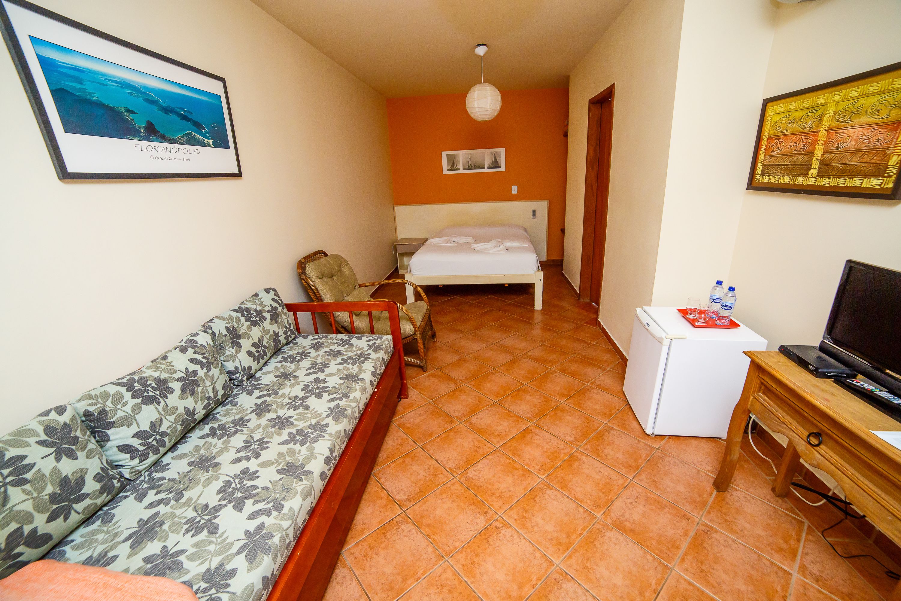 A room with a bed, a sofa, a small table with a TV, and a refrigerator.