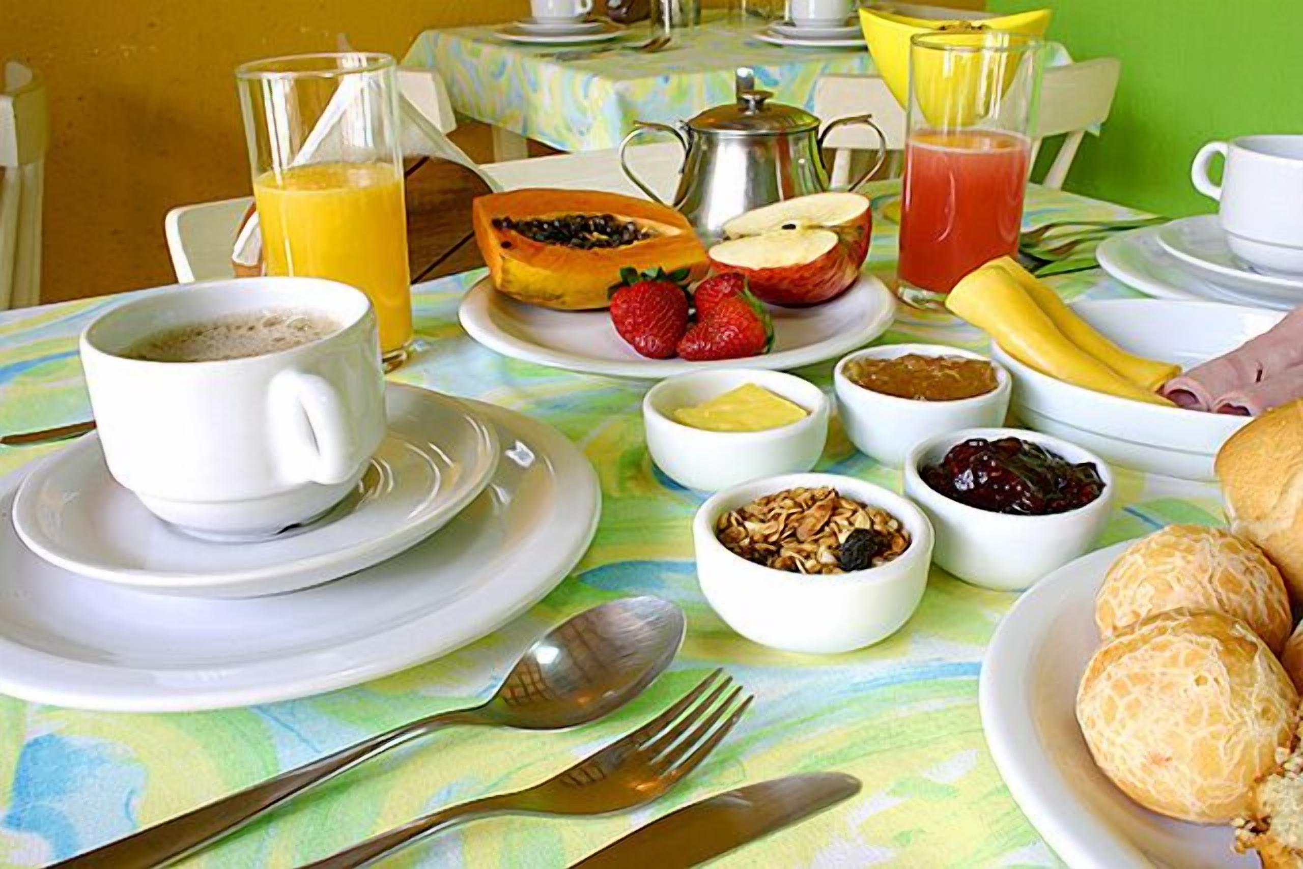 A breakfast table with plates of food, a coffee cup, and a fruit bowl.
