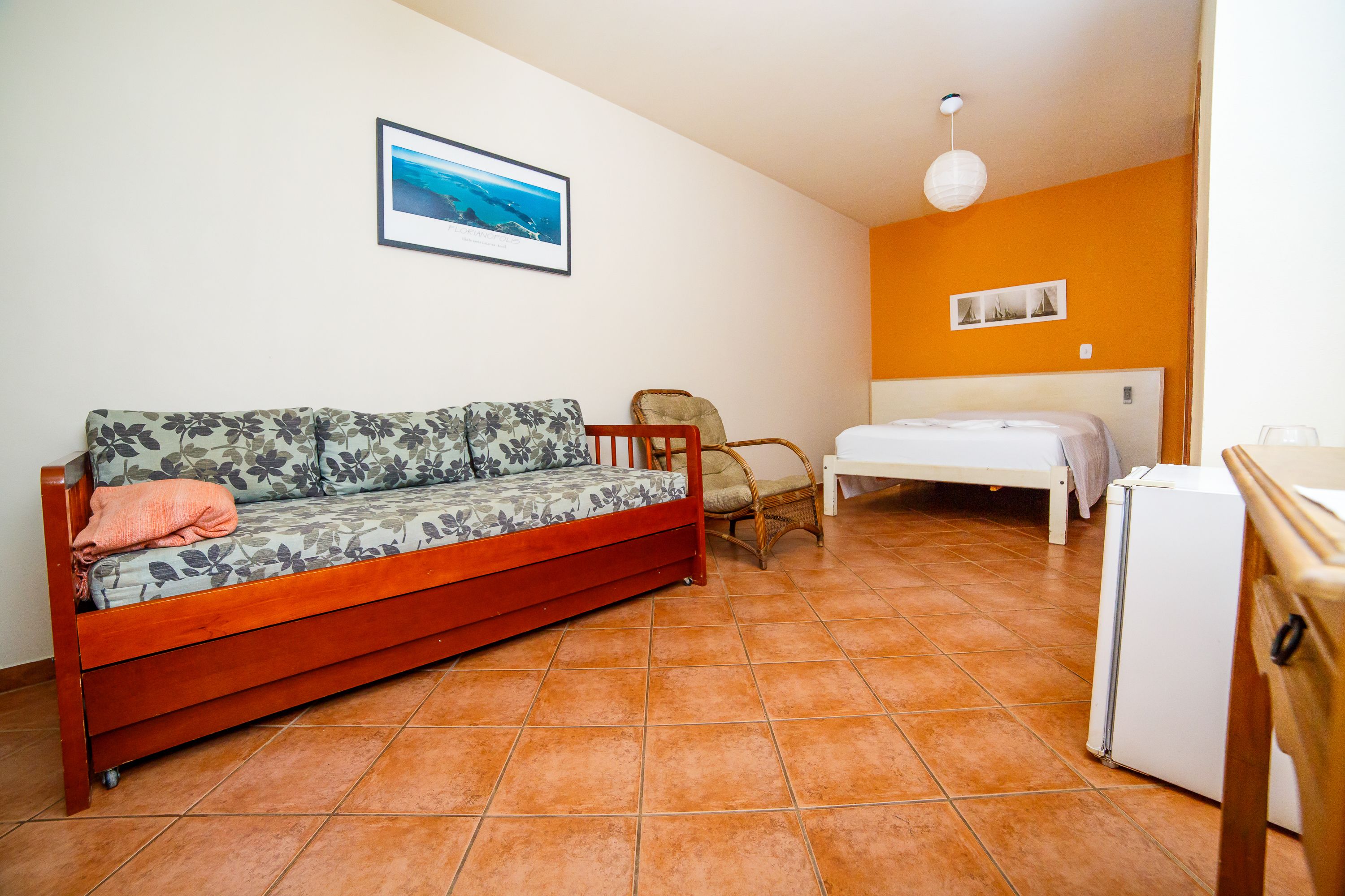 Una habitación con sofá, sillón, cama y refrigerador.