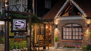 A cozy restaurant with a brick exterior, a wooden bench, and a signboard. - Pousada Caliandra da Serra (Canela)