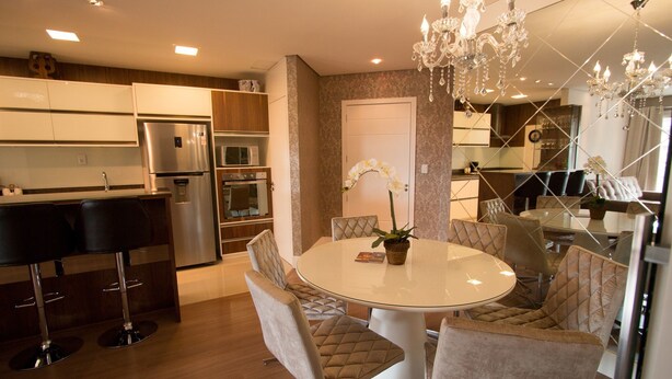 A modern kitchen with stainless steel appliances, a dining area with a round table and cushioned chairs, and a chandelier. - Residencial Florence (Gramado)