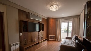 A modern living room with a wooden entertainment unit, a large flat-screen TV, a sofa, and a decorative ceiling light. - Residencial Florence (Gramado)