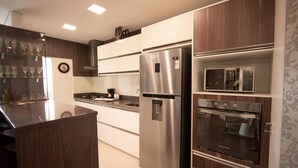 A modern kitchen with stainless steel appliances, wooden cabinets, and a built-in microwave. - Residencial Florence (Gramado)