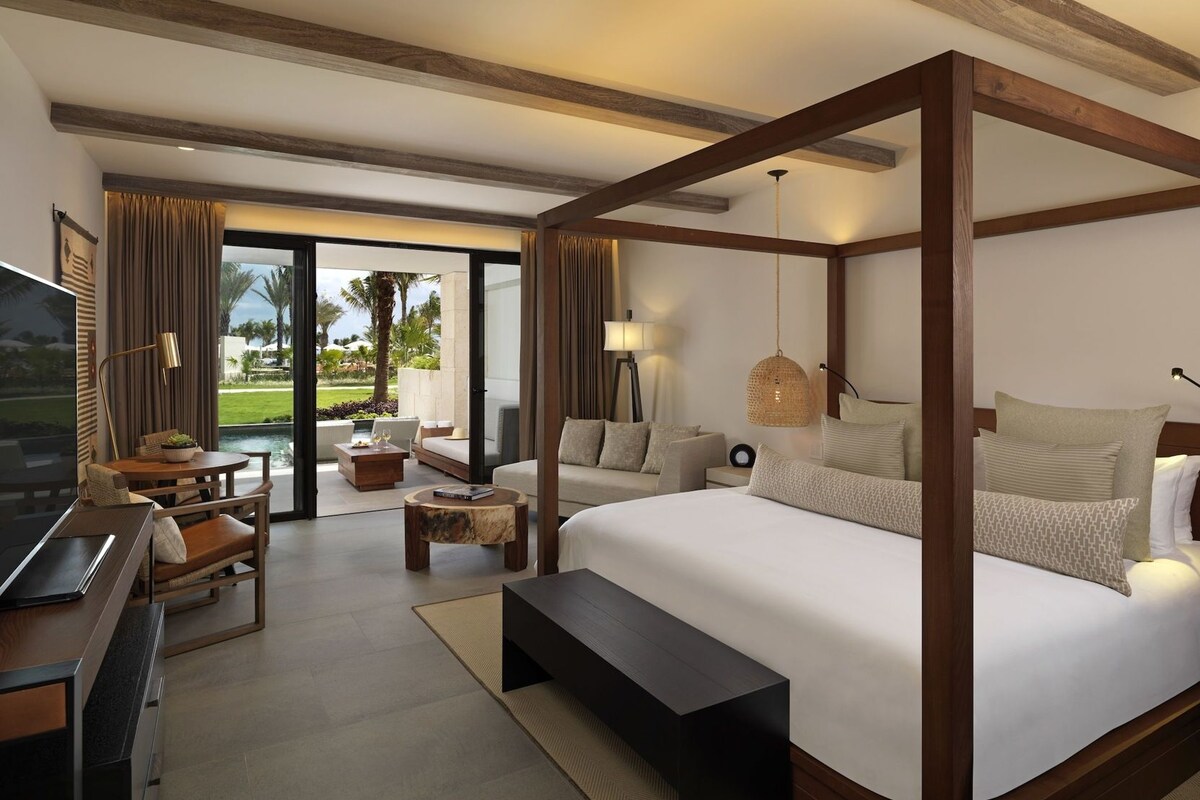 Quarto de hotel com uma cama grande, uma escrivaninha, televisão e vista para um jardim.
