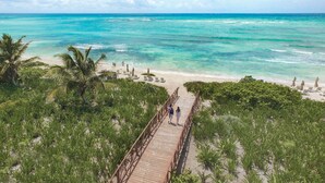 A wooden boardwalk leading to a beach with clear turquoise water and palm trees.