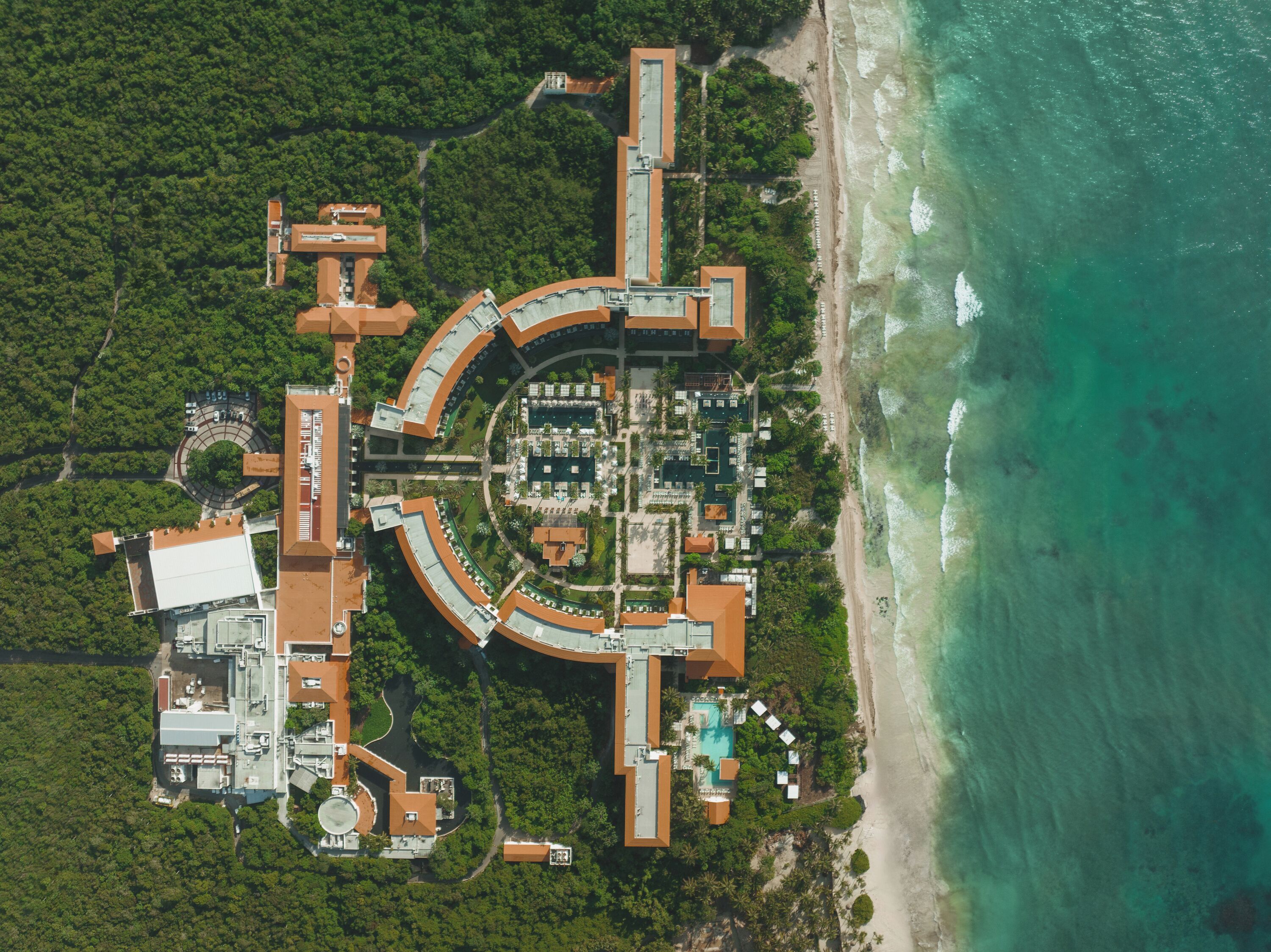 Vista aérea de un complejo turístico con un edificio circular central, una playa y una zona de piscina.