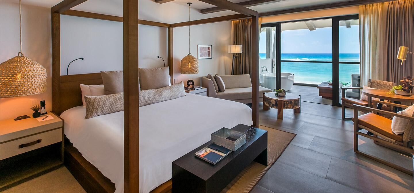 A spacious bedroom with a four-poster bed, a sitting area with a view of the ocean, and a balcony with a view of the sea.